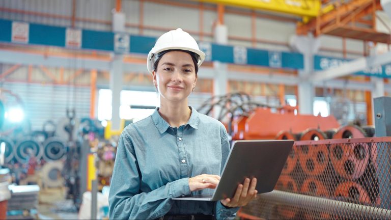 A construction engineer in the field, looking at us, with a laptop in her hands